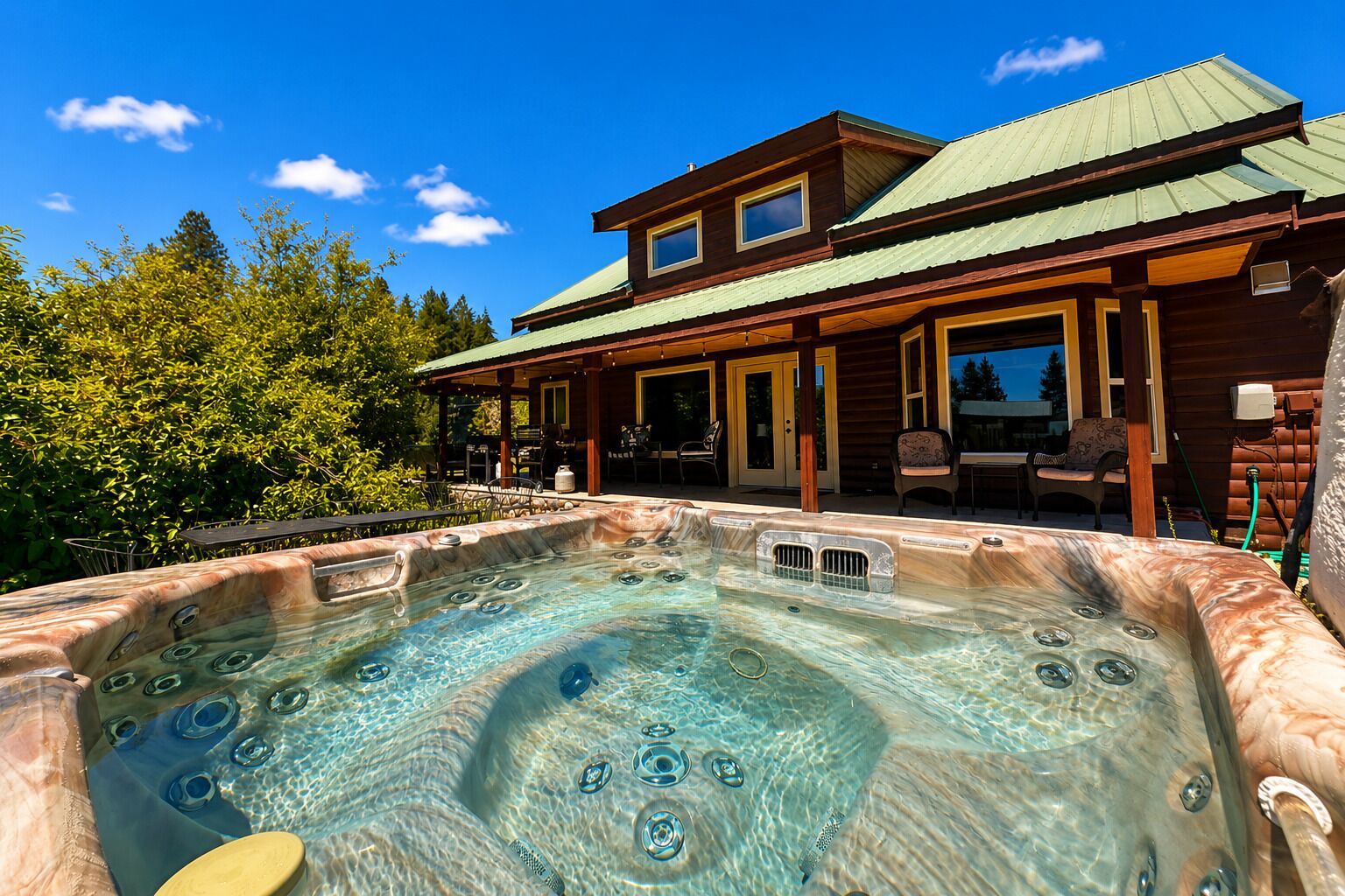 A hot tub with a wooden deck, a covered patio, and a two-story building with a green roof.