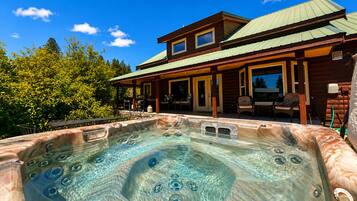 A hot tub with a wooden deck, a covered patio, and a two-story building with a green roof.