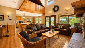 A spacious living area with a high ceiling, wooden beams, a fireplace, and a view of the outdoors.