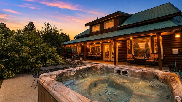 A hot tub in front of a wooden cabin with a covered patio and outdoor seating.