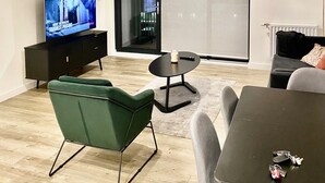 A modern living room with a flat-screen TV, a green armchair, a grey sofa, and a dining table. - Captivating 2-bed Apartment in London (London)