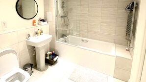 A modern bathroom with a toilet, sink, mirror, and a glass-enclosed shower area. - Captivating 2-bed Apartment in London (London)