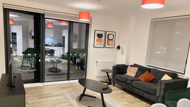 A modern living room with a sofa, a coffee table, and a TV. There is a sliding glass door leading to a balcony with outdoor furniture. - Captivating 2-bed Apartment in London (London)