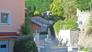 A residential building with a stone staircase leading to a second-floor entrance, surrounded by lush greenery and a stone wall. - Bruk in Lovran - Kvarner Region / Bruk in Lovran - Appartement für 2 Personen AP2 (Lovran)