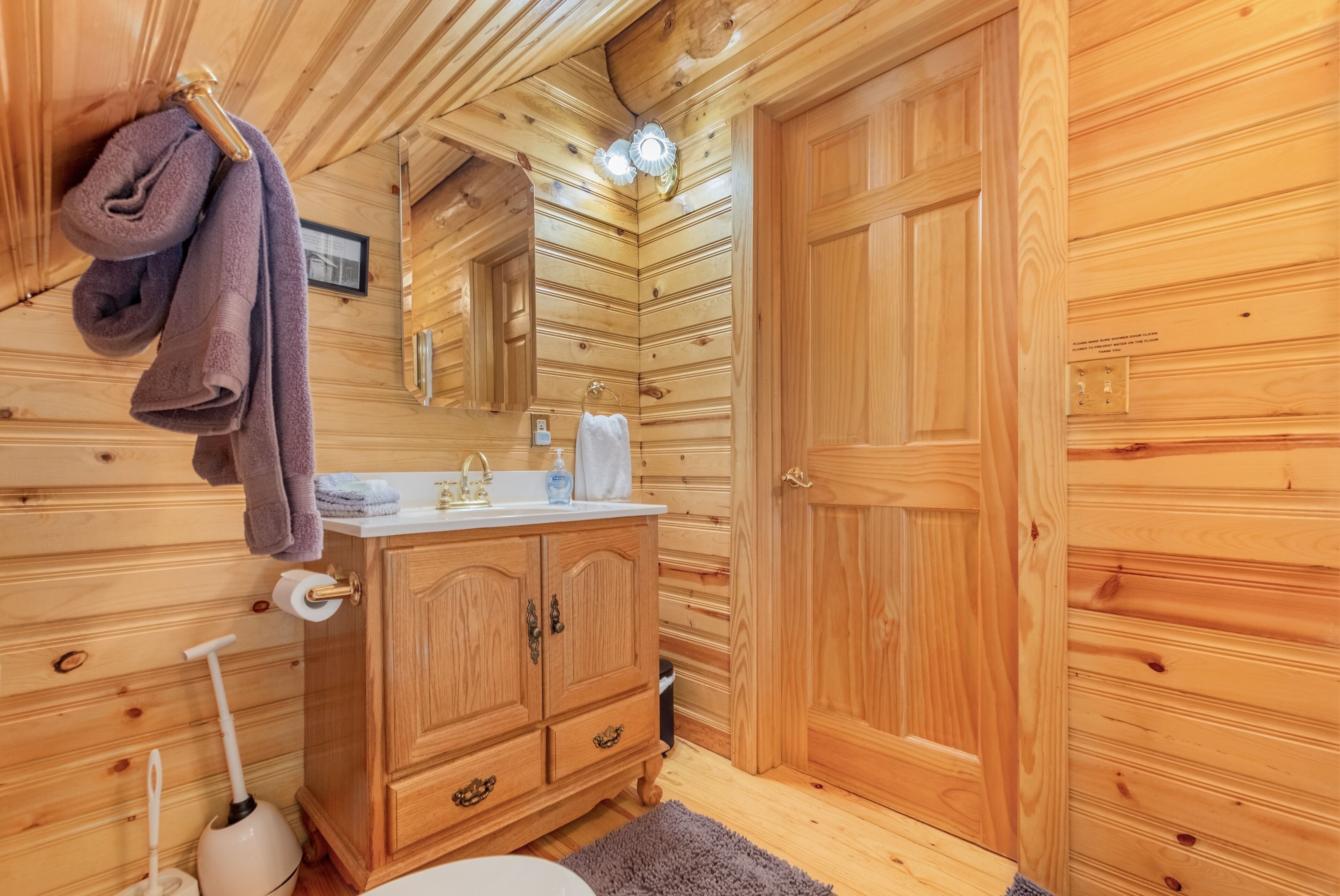 A wooden cabin bathroom with a wooden vanity, a mirror, a towel rack, and a toilet.