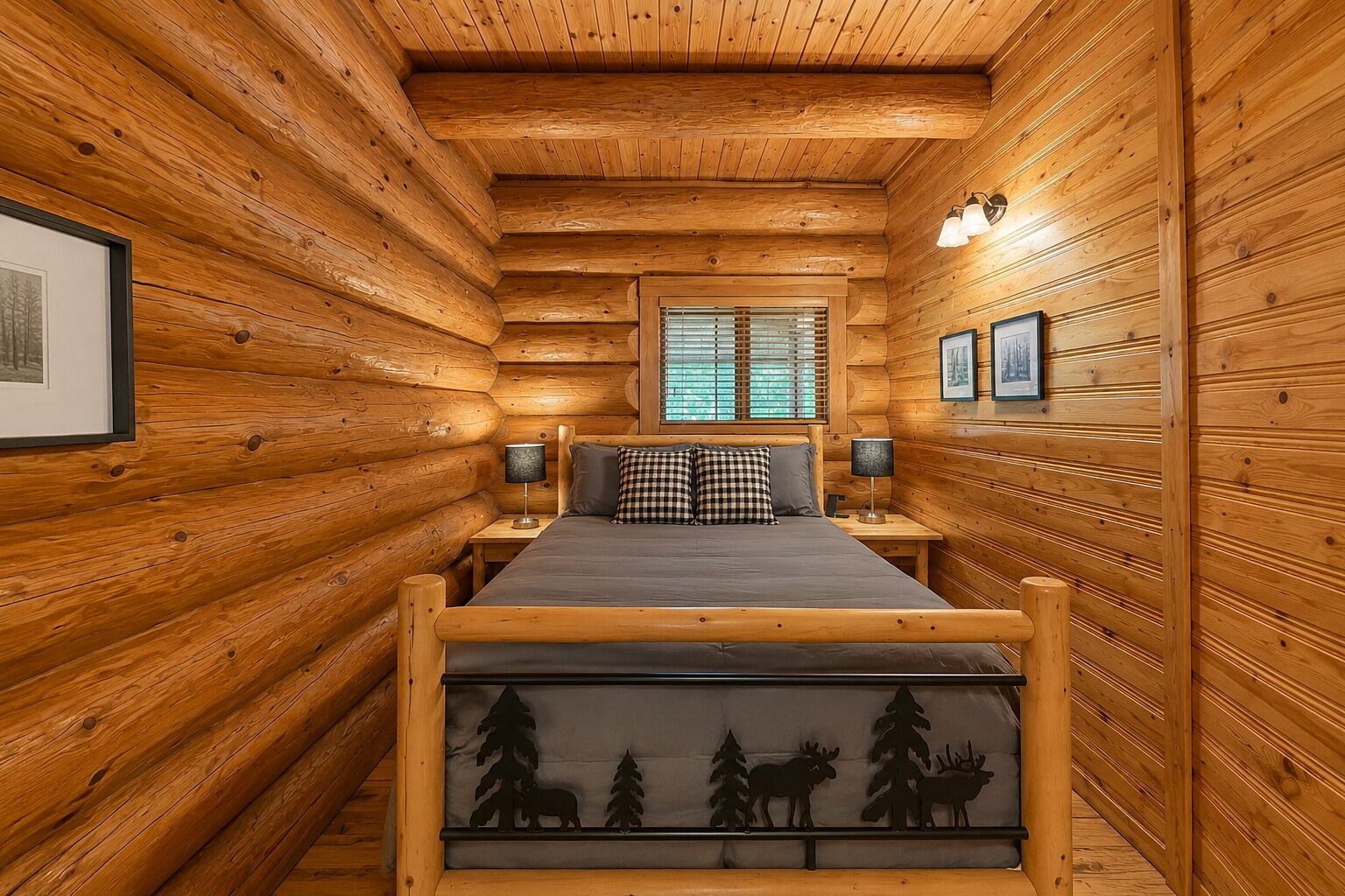 A log cabin bedroom with a bed, two bedside lamps, a window with blinds, and framed pictures on the walls.