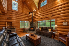 A log cabin interior with a stone fireplace, leather furniture, and large windows. - Soaring Pines Lodge 1 Bedroom Home by NW Comfy Cabins by RedAwning (Leavenworth)