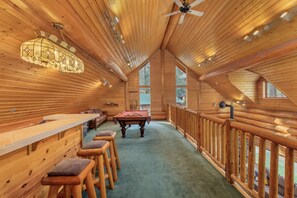 Un intérieur en bois comprenant une table de billard, un bar et un espace détente avec des sièges.