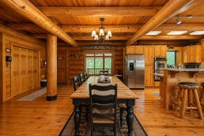 A log cabin interior with a dining table, chairs, a chandelier, a kitchen area, and a large window. - Soaring Pines Lodge 1 Bedroom Home by NW Comfy Cabins by RedAwning (Leavenworth)