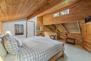 Une chambre confortable avec un plafond en bois, un lit recouvert d’une couette à carreaux, un bureau et une chaise.