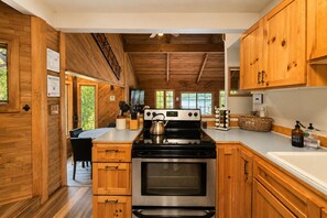 Une cuisine moderne avec des meubles en bois, une cuisinière en acier inoxydable et une grande fenêtre donnant sur un paysage naturel.