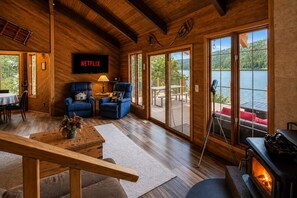 Un intérieur de chalet chaleureux avec une cheminée, un logo Netflix et une vue pittoresque sur un lac.