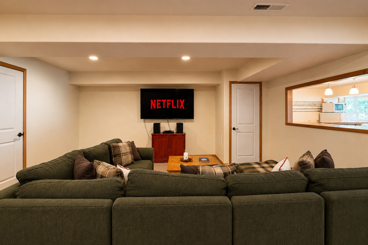 A living room with a sectional sofa, a coffee table, and a wall-mounted TV displaying 'NETFLIX'.