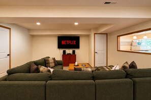 Un salon comprenant un canapé d’angle, une table basse et un téléviseur fixé au mur qui affiche le logo « NETFLIX ».