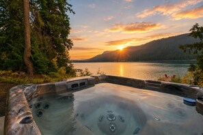 Een hottub met uitzicht op een meer en bergen tijdens zonsondergang.