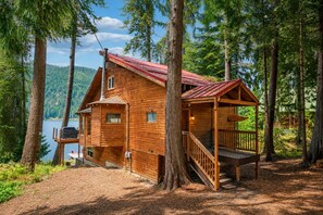 Eine Holzhütte mit Terrasse, umgeben von Bäumen und einem See.