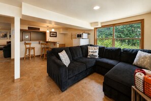 Un salon moderne avec un canapé d’angle, un coin repas doté d’un bar et une grande fenêtre donnant sur un paysage verdoyant.