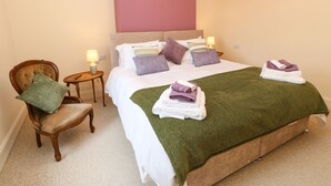 Ein ordentlich eingerichtetes Hotelzimmer mit einem großen Bett, einem Sessel, einem kleinen Tisch und einer Lampe.