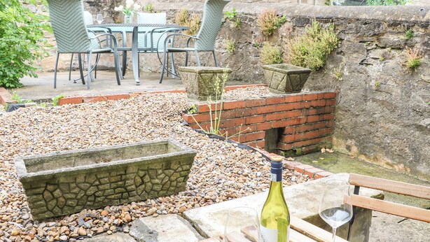 Eine Terrasse mit Tisch und Stühlen, einem Steinpflanzgefäß und einer Weinflasche.