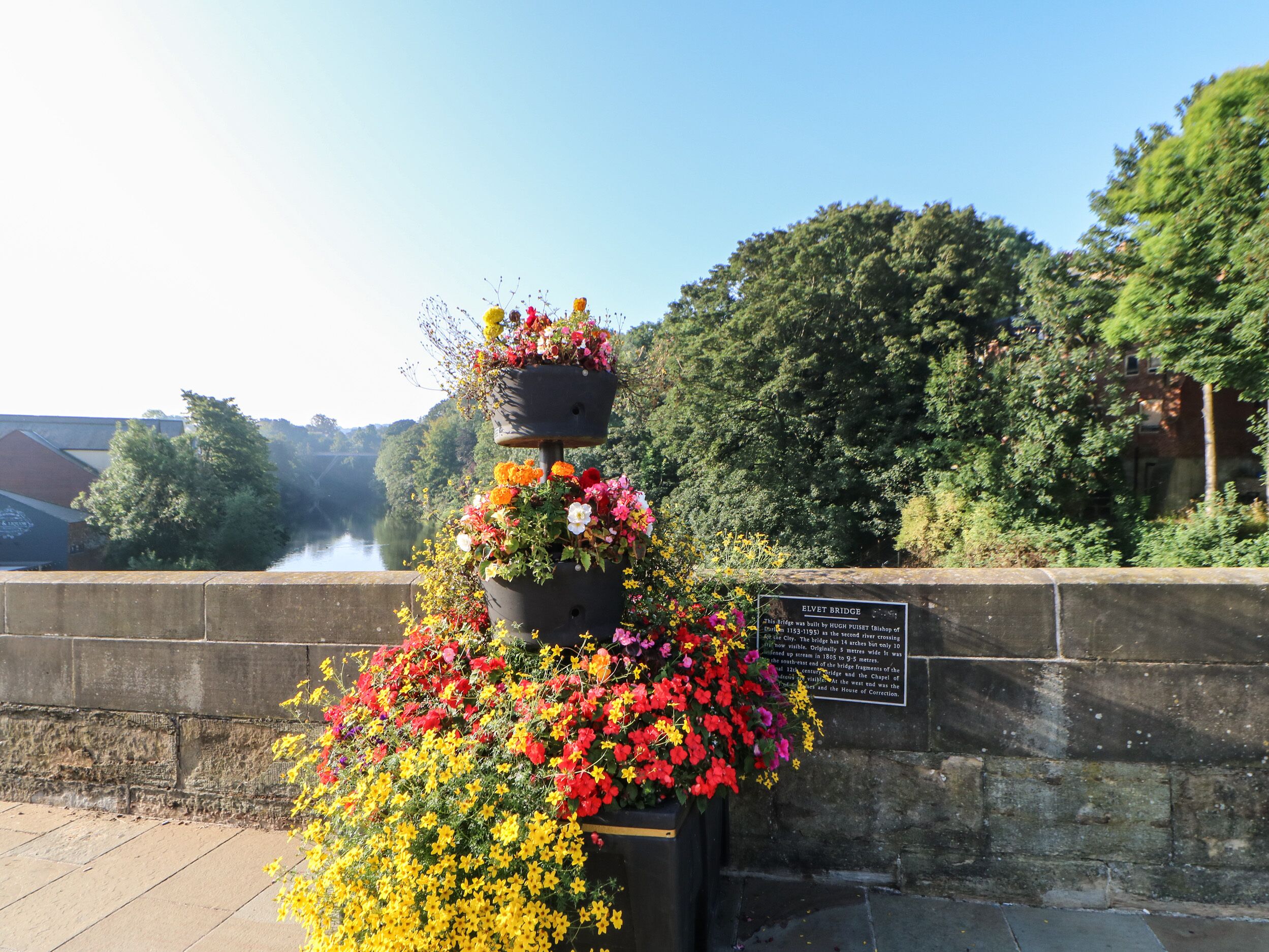 A tiered flower arrangement with a plaque beside a stone wall.