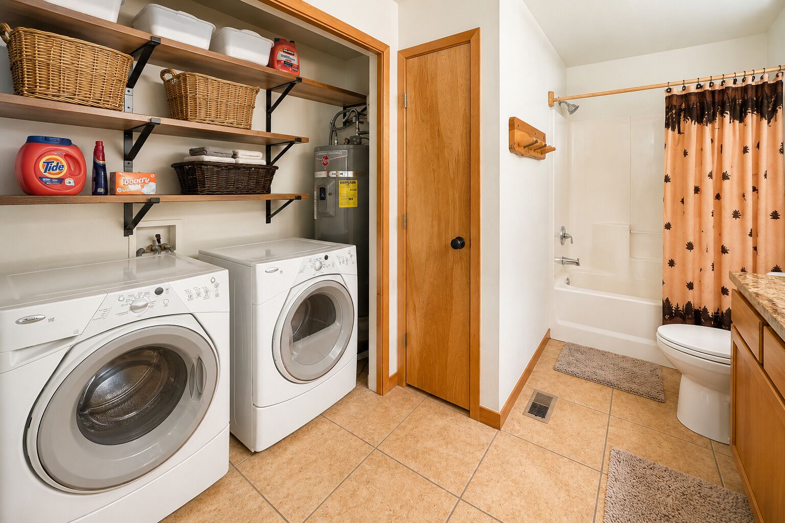 Ein Waschraum mit zwei Frontlader-Waschmaschinen, Regalen mit Körben und Reinigungsmitteln, einer Holztür, einer Duschkabine und einer Toilette.