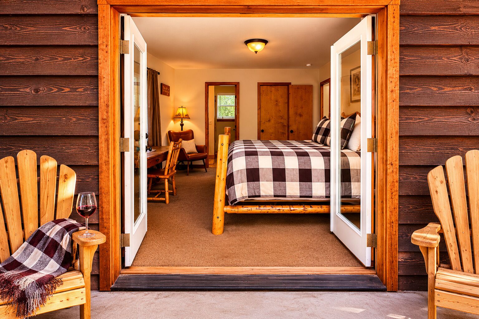 A wooden cabin interior with a bed, chairs, a table, and a glass of wine.