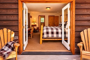 A wooden cabin interior with a bed, chairs, a table, and a glass of wine.