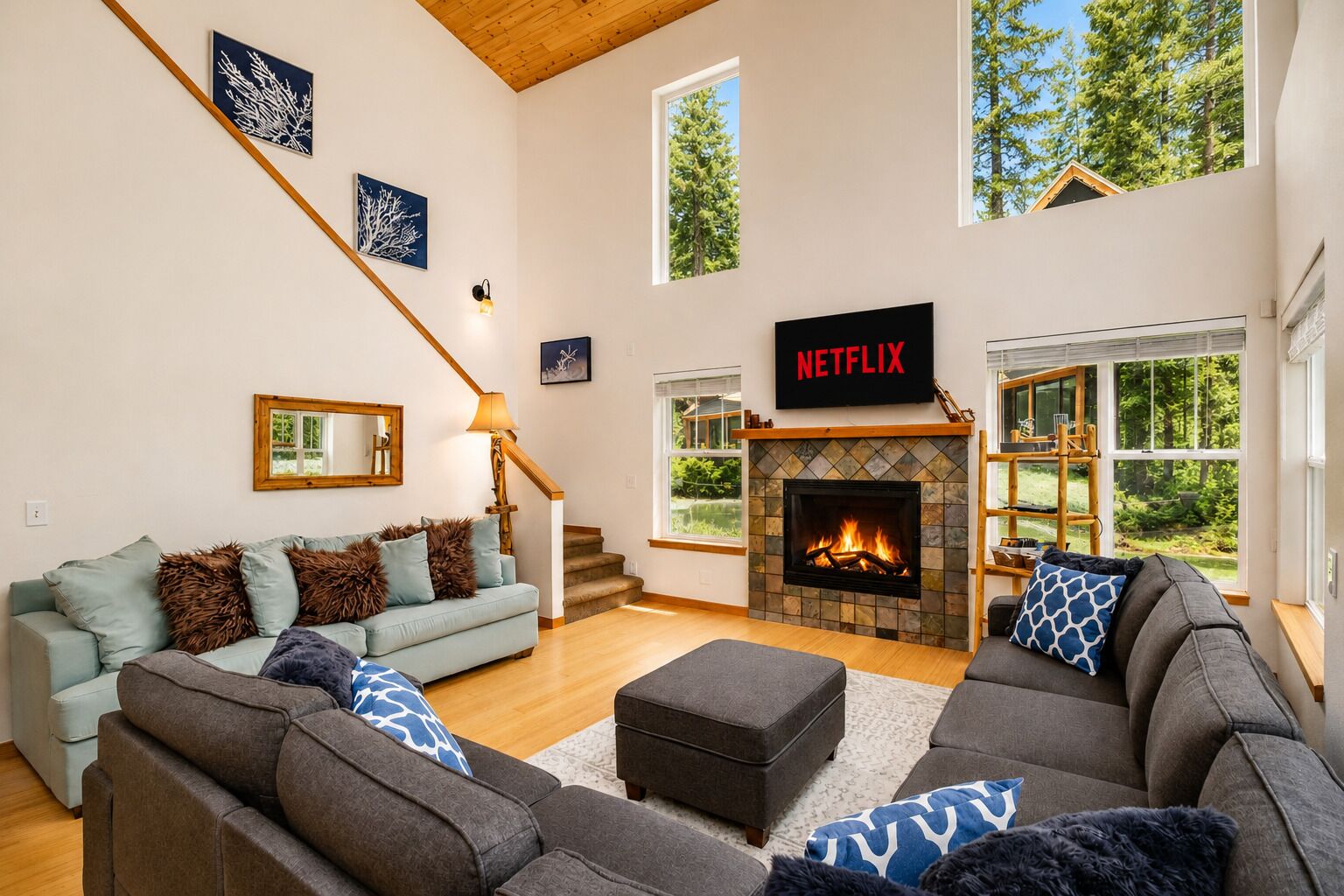 A spacious living room with a fireplace, a staircase, and a large window offering a view of trees.
