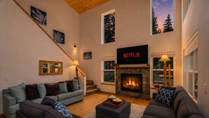 Een woonkamer met een open haard, een Netflix-bord, een trap en een groot raam.
