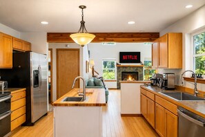 Una cocina moderna con armarios de madera, un refrigerador de acero inoxidable, una isla integrada con pileta y una chimenea.