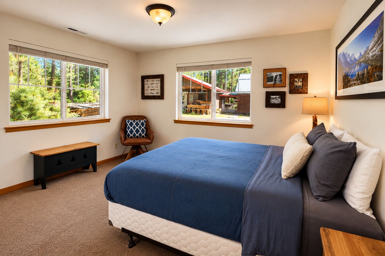 A bedroom with a bed, a bench, a chair, and two windows offering a view of the outdoors.