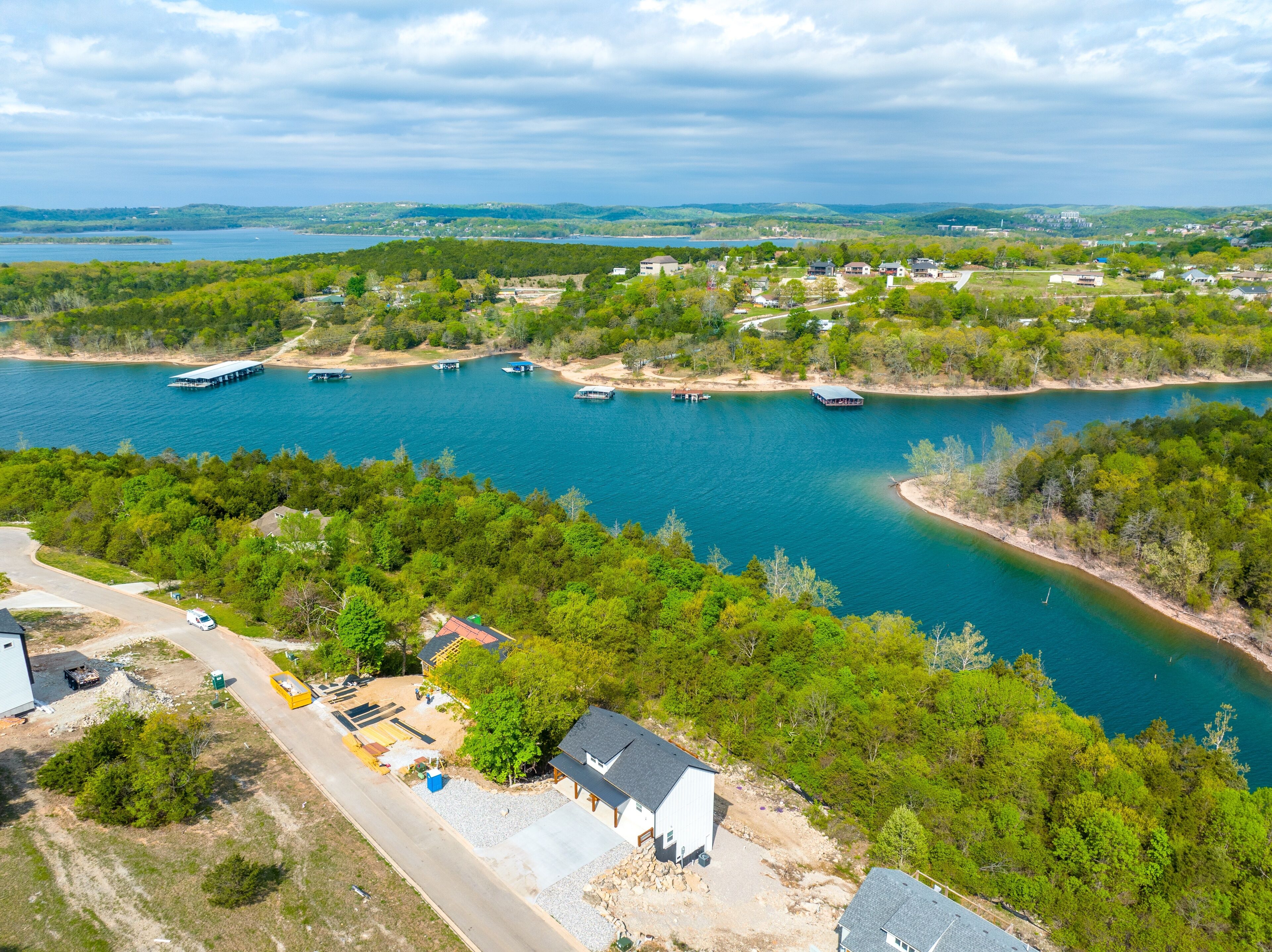 An aerial view of a riverside property with boats docked, a road, and a mix of residential and commercial buildings.