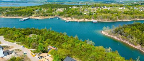 An aerial view of a riverside property with boats docked, a road, and a mix of residential and commercial buildings.