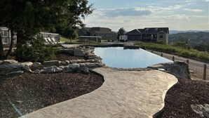 En swimmingpool med en kant av sten, omgiven av ett vackert anlagt område med träd och utsikt över hus i bakgrunden.