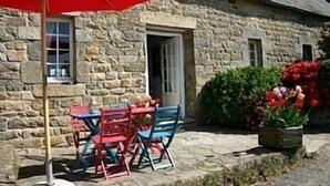 A stone building with a door and windows, a red umbrella, and a table with chairs outside. - NEW: Ker Louarn (Ploubezre)