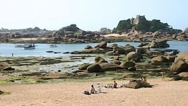 A rocky beach with large boulders and a castle in the background. - NEW: Ker Louarn (Ploubezre)