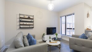 Een moderne woonkamer met een bank, een salontafel, een televisie en een raam met jaloezieën.