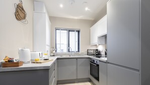 Een moderne keuken met grijze kastjes, een ingebouwde oven en een raam met zonwering.