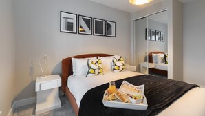 Een moderne hotelkamer met een net opgemaakt bed, een nachtkastje met lamp, een dienblad met ontbijtartikelen en een grote spiegel.