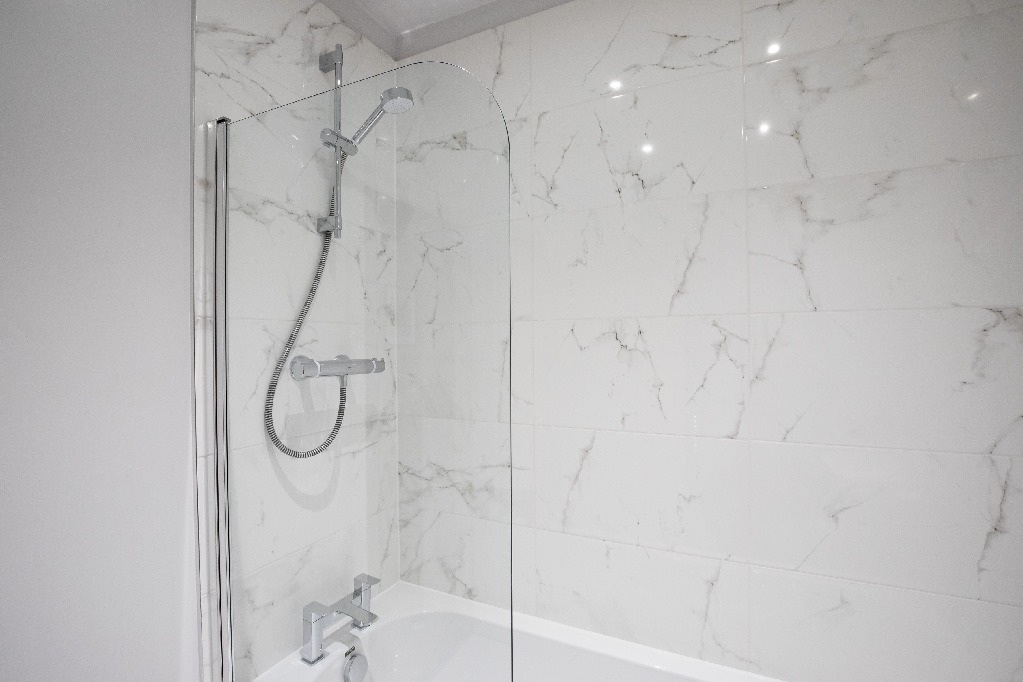 Een moderne badkamer met een douchecabine, een badkuip en marmeren wanden.