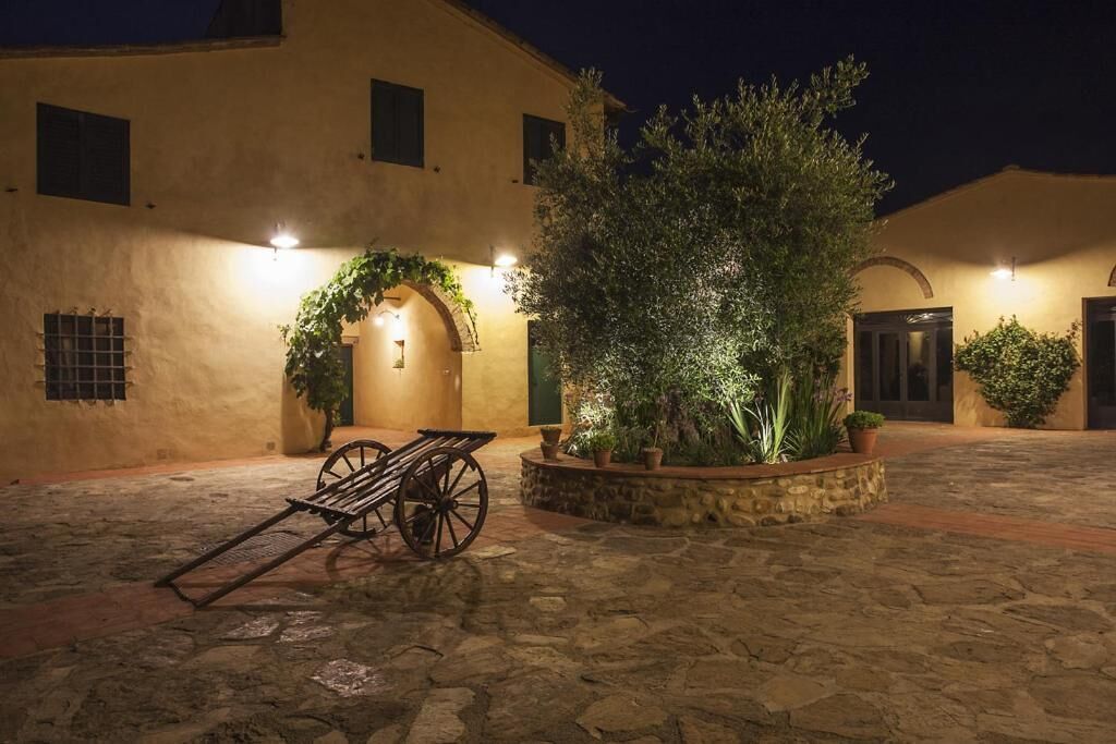 Un patio con suelo de piedra, un carro de madera y un edificio con entrada iluminada.