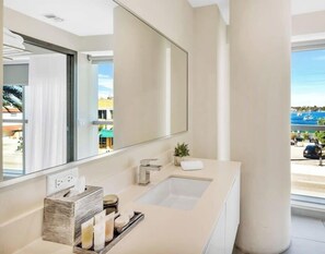 A modern bathroom with a large mirror, a sink, and a window offering a view of the outside.