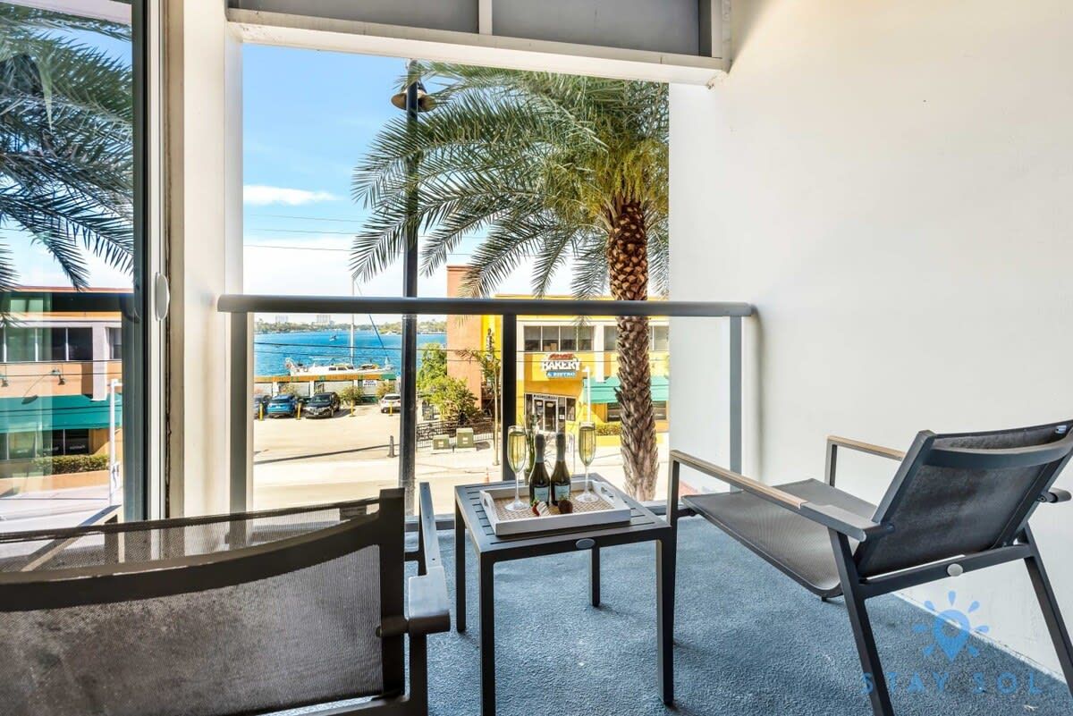 Un balcon avec une table dressée pour deux personnes, une chaise et une vue sur la rue et l’océan.