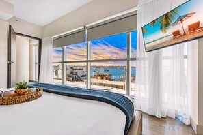 A hotel room with a large bed, a TV, and a view of the sea.