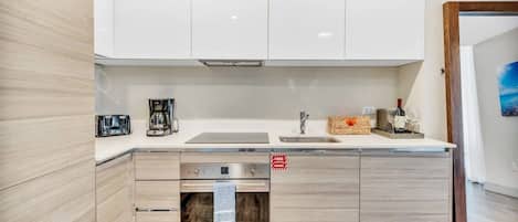 Una cocina moderna con armarios blancos, horno empotrado y un lavamanos.