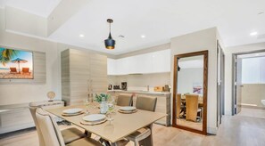 A modern dining area with a wooden table set for four, beige chairs, and a pendant light.