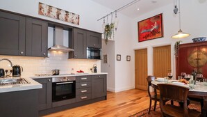 A modern kitchen with dark cabinets, a Bosch oven, and a dining area with a wooden table and chairs. - Ebenezer Chapel (Saxmundham)