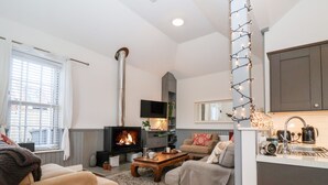 A cozy living room with a fireplace, comfortable seating, and a kitchen area. - Ebenezer Chapel (Saxmundham)