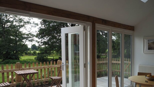 A room with a wooden table and chairs, a sliding glass door leading to a garden with a wooden fence. - Historic remodelled stable barn near nature conservation (Pulborough)