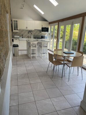 A modern kitchen with white cabinets, a central island, and a dining area with chairs and a table. - Historic remodelled stable barn near nature conservation (Pulborough)